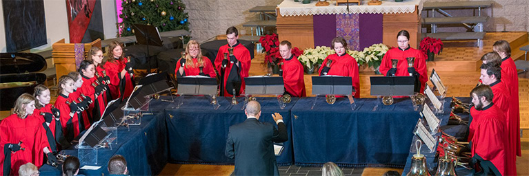 A handbell choir in red robes performs in a church, engaging students within the Mankato campus community.