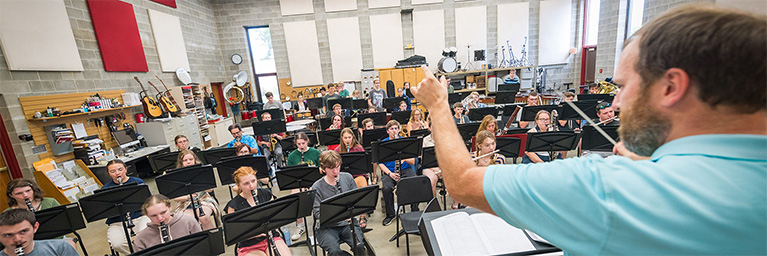 A music teacher in Minnesota leads a large group of students who are playing instruments together, increasing student engagement.