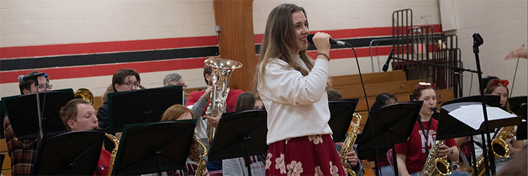 A Bethany Lutheran College student sings into a microphone while the school band performs in a Mankato gymnasium.