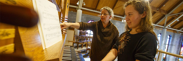 Two women at an organ in Bethany Lutheran College’s campus chapel; one points at sheet music while the other plays.