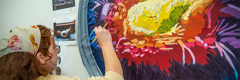 A person paints a vibrant, colorful abstract design on a large circular canvas in an art studio in Minnesota.