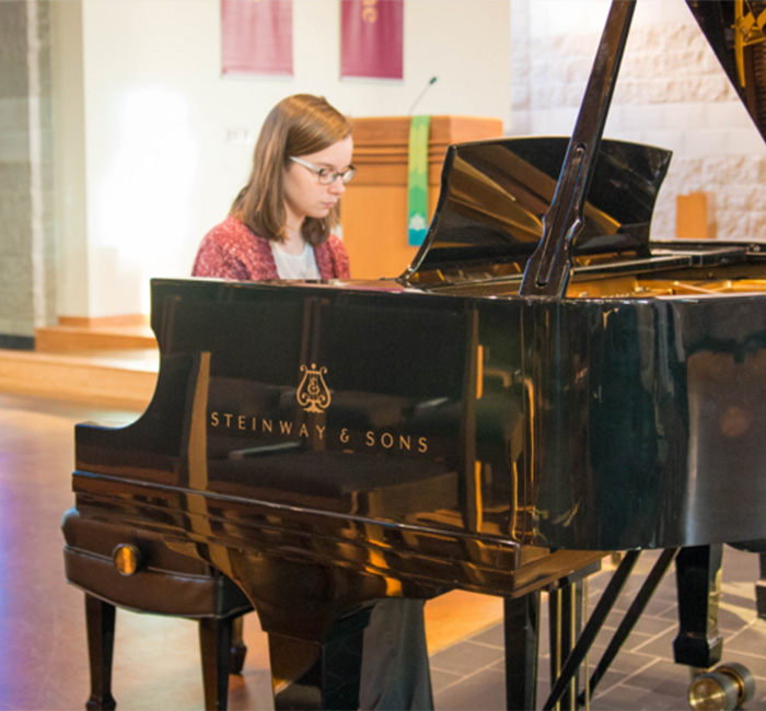 A Bethany Lutheran College student with glasses plays a black Steinway & Sons grand piano in Minnesota.