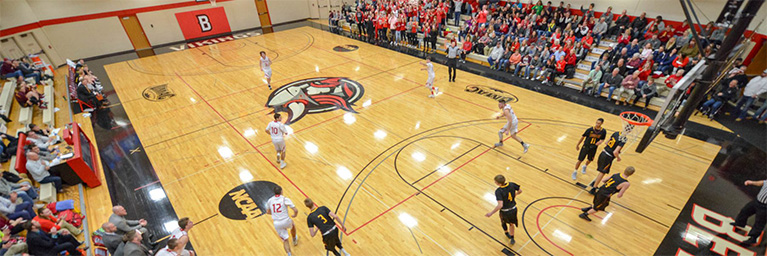 Aerial view of a basketball game in Mankato, with members of the campus community cheering from the gym bleachers.