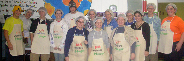 A group of smiling volunteers from the campus community stands together in front of a colorful mural.