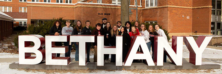 A group of students stands behind large BETHANY letters on the snowy campus of Bethany Lutheran College in Mankato, Minnesota.