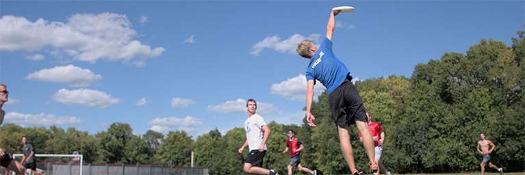 Bethany Lutheran College students play ultimate frisbee on a grassy field under a blue sky, promoting student engagement.