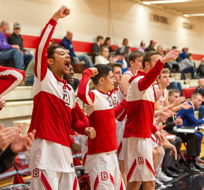 Bethany Lutheran College students in red and white uniforms enthusiastically cheer and celebrate during a basketball game in Minnesota.