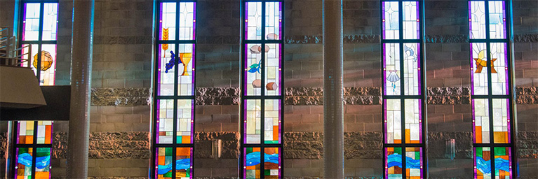 Tall stained glass windows line the brick-walled interior, creating a vibrant atmosphere for student engagement at Bethany Lutheran College.