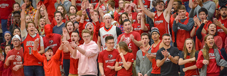 A group of enthusiastic Mankato students wearing red shirts cheer and clap at a sports event, demonstrating strong student engagement.