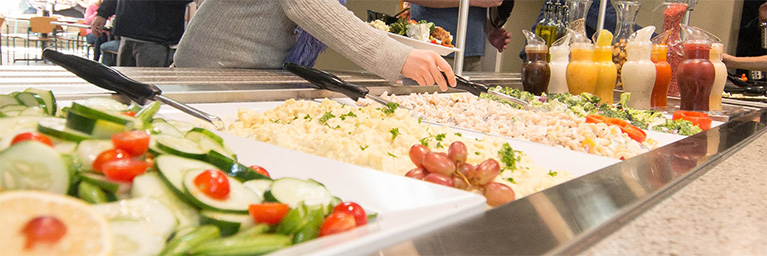 A person serves food from a buffet featuring salads and pasta at a student engagement event in Mankato, Minnesota.