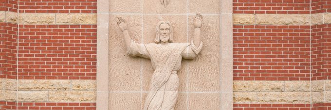 Stone relief depicting a robed figure with raised arms, set within a brick and stone wall.