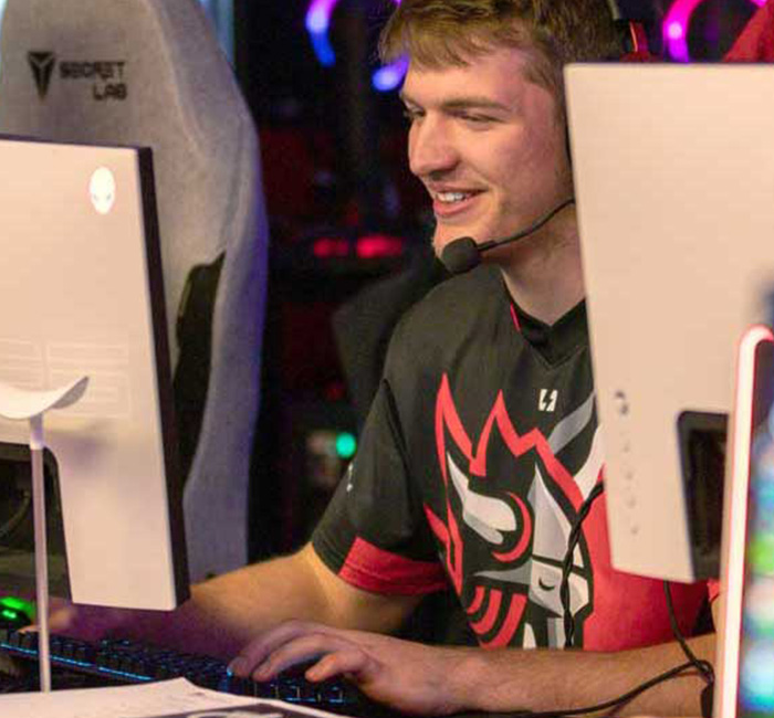 A young man wearing a headset smiles as he plays on a computer at a gaming event.