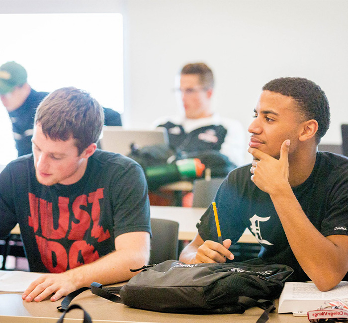 Two male students at Bethany Lutheran College in Mankato, Minnesota, sit at desks; one writes while the other looks ahead.
