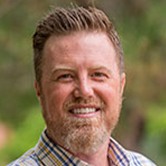Chris Bollig, Adjunct Faculty for the Clinical Mental Health Counseling – Graduate Programs Department, stands outdoors with greenery in the background.