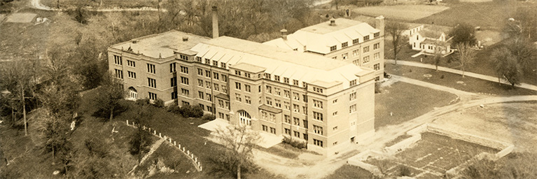 A sepia-toned aerial view of Bethany Lutheran College’s historic brick building, surrounded by trees and open land.