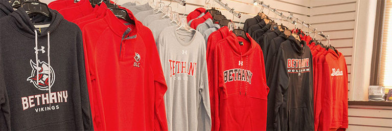Red, gray, and black Bethany Lutheran College hoodies and sweatshirts are displayed on hangers in a community store on the Mankato campus.