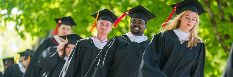 Bethany Lutheran College graduates walk outdoors in caps and gowns, smiling and celebrating as they participate in commencement.