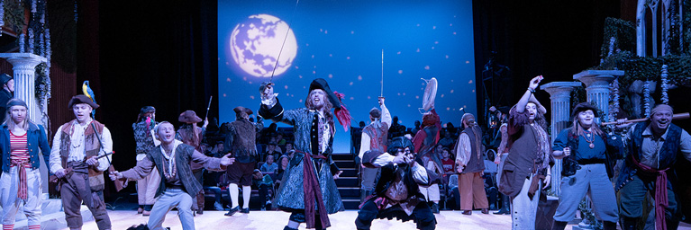 Bethany Lutheran College students perform on stage in pirate costumes, with a moonlit sky projected in the background.