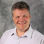Brian Klebig, Professor for the Communication Department, against a gray backdrop.