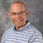 Chad Heins, Associate Professor for the Biology Department, posed in front of a gray background.