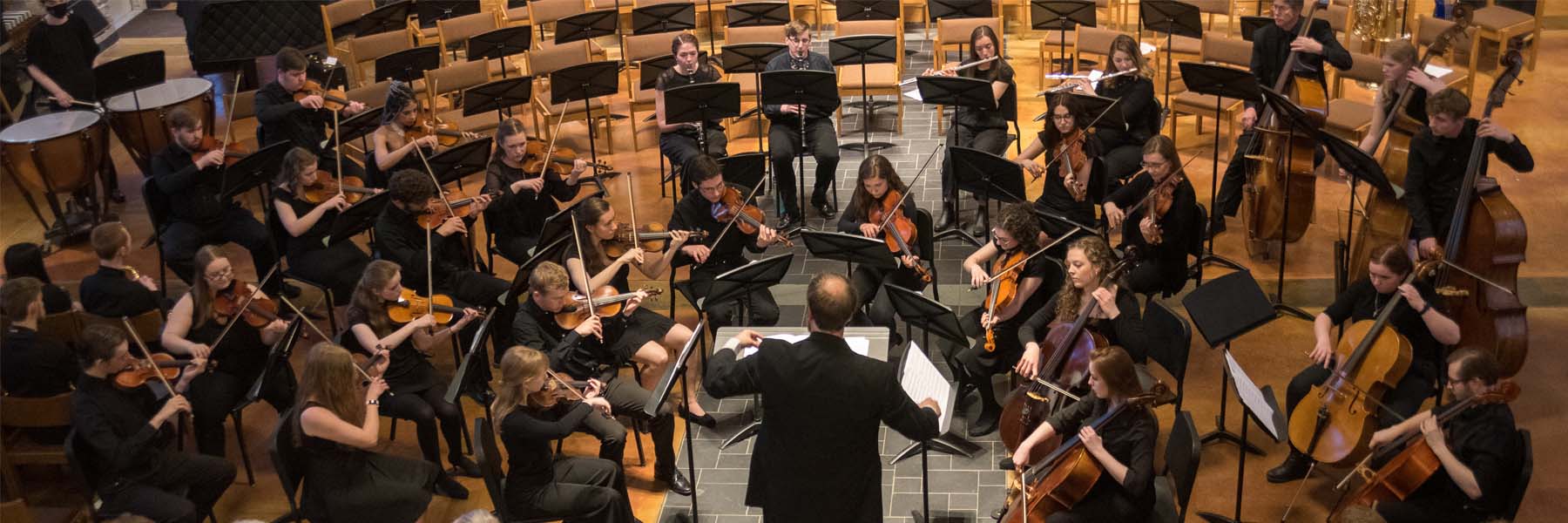 A conductor leads an orchestra of musicians, engaging students in Bethany Lutheran College’s concert hall.