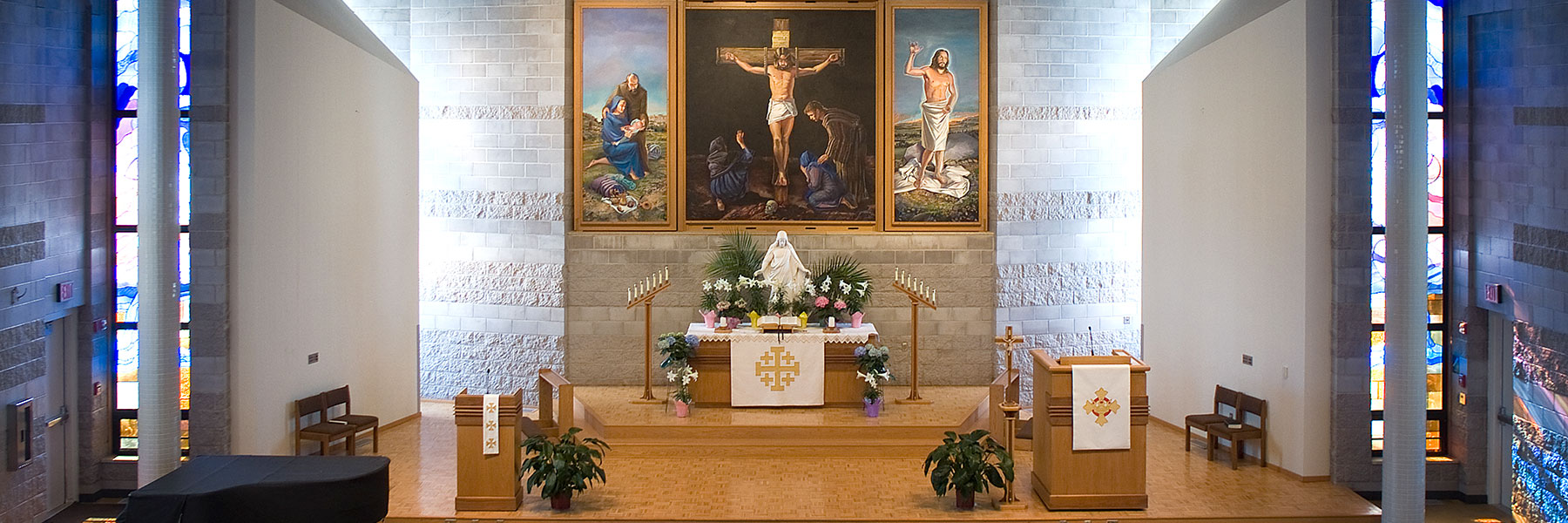 A church altar with candles, flowers, and a white cloth stands beneath paintings of the crucifixion in Mankato’s campus community.