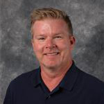 Christopher Kind, Director of the Advancement Department, posed on a gray backdrop.