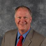 Daniel Mundahl, Senior Vice President of Finance and Administration for the Finance and Administration Department and Online Instructor for the Broad Field Social Studies Department, poses in front of a mottled gray background at the Mankato campus community.