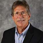 Dave Urness, String Instructor for the Music Department, poses in front of a gray background.