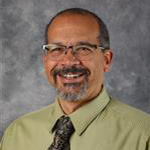David Paulson, Assistant Professor for the Music Department, against a gray backdrop.