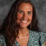 Denice Woller, Adjunct Faculty of Studio Art Department, smiling in front of a gray mottled background.