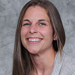 Emma Purfeerst, Head Coach Women's Basketball of the Athletics Department and Adjunct Faculty for the Biology Department, standing in front of a textured gray background.