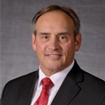 Gene Pfiefer, President of the College for the President's Office Department, standing against a gray backdrop.
