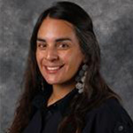 Helena Stevens, Associate Professor for the Clinical Mental Health Counseling – Graduate Programs Department, smiles in front of a gray mottled background.