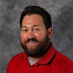 Jake Krier, Director of Alumni Relations for the Advancement Department, poses at Bethany Lutheran College in front of a gray background.
