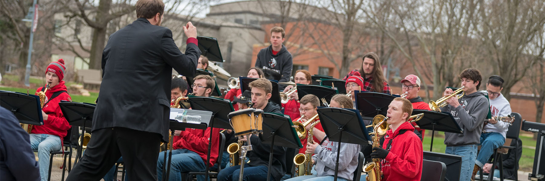 A band conductor leads students from the campus community as they play brass and woodwind instruments outdoors at Bethany Lutheran College.