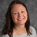 Jen Kom, Professor for the Psychology Department, posing in front of a grey backdrop.