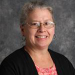 Laura Matzke, Organ, Piano, and Voice Instructor for the Music Department, standing against a gray background.