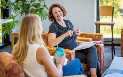 Two women sit in armchairs, chatting and smiling in a bright room at Bethany Lutheran College.