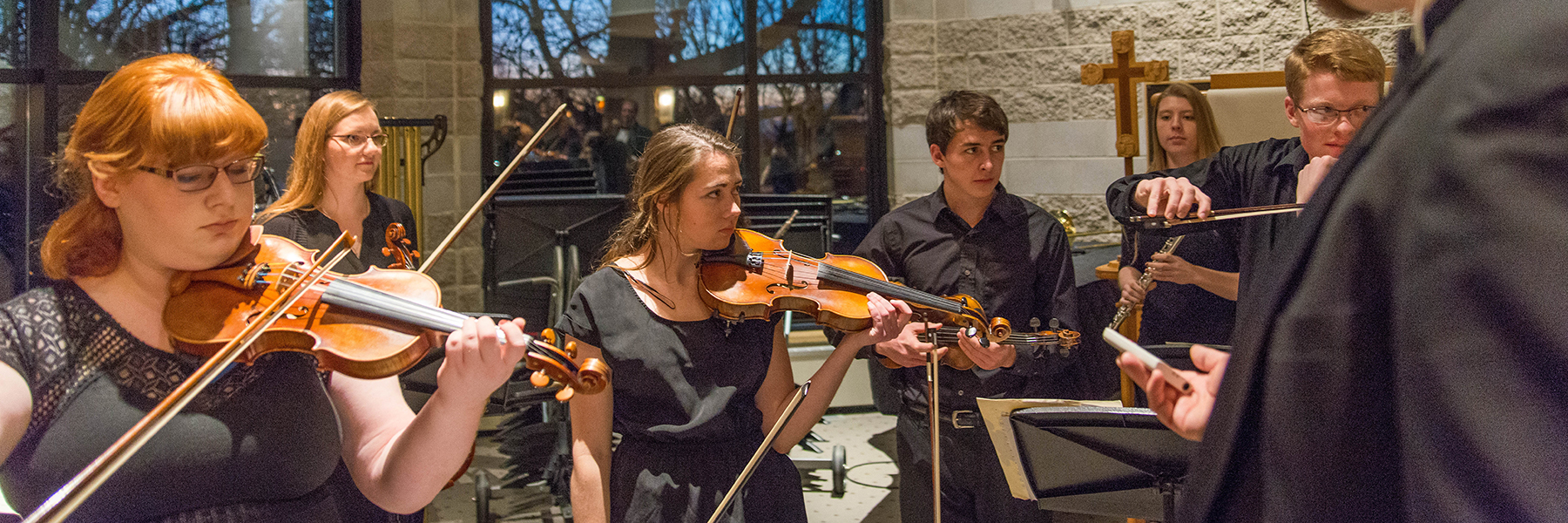 A group of musicians wearing black outfits play violins together in a stone-walled room in Mankato, Minnesota.