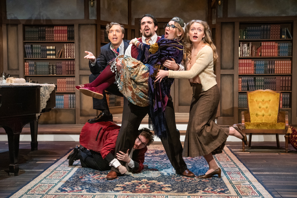 Five actors on stage at a Minnesota campus community strike dramatic and comedic poses; one actor is lying on the floor.