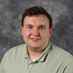 Nicolas Lewison, Resident Hall Coordinator for the Residential Life Department, poses in front of a gray mottled background.