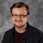 Noah Dale, Housekeeping Technician for the Housekeeping Department, smiling in front of a gray background.
