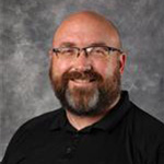 Patrick Langworthy, Housekeeping Technician for the Housekeeping Department, smiles in front of a gray background.
