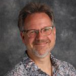 Peter Blowdel, Professor for the Theatre Department, stands against gray background.
