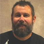 Peter Schuch, Housekeeping Technician for the Housekeeping Department, stands against tan background.