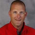 Ryan Kragh, Co-Athletic Director and Head Baseball Coach for the Athletics Department, smiles slightly in front of a gray background.