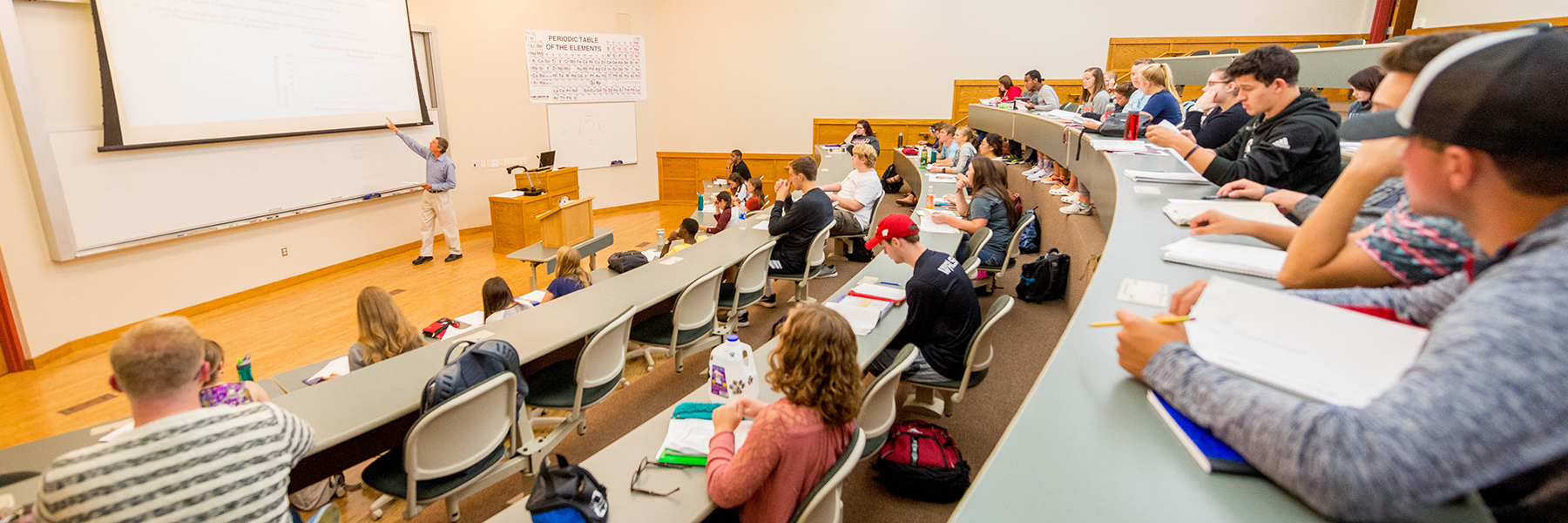 A professor lectures to students in a tiered Mankato classroom, while the students take notes and listen attentively.