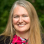 Stacey Dawley, Director of Finance & Business Affairs for the Finance and Administration Department, standing outdoors among greenery.