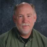 Tom Bierer, Lessons Instructor for the Music Department, poses in front of a gray background at Bethany Lutheran College.